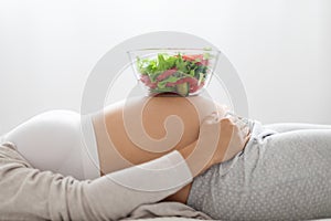 Bowl with fresh salad on pregnant woman belly