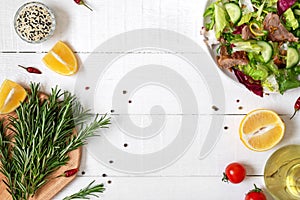 Bowl of fresh salad, rosemary, lemon, spices and oil on white wooden table. Food background.