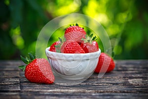 Bowl of fresh strawberries on wooden table in summer garden