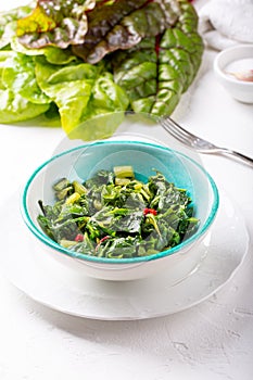 Bowl of fried chard leaves on white background. Vegetarian or vegan diet, healthy food concept