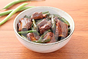 Bowl of fried pork ribs with green bean on wooden table