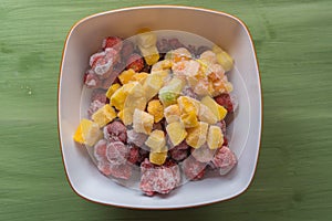 Bowl with frozen fruit chunks on green wooden table