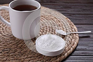 Bowl of fructose powder and cup with tea on dark wooden table