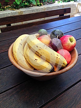 Bowl of fruit including bananas, apples and passion fruit on an outdoor wooden table