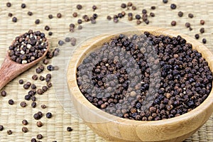 Bowl full of black peppercorns on a bamboo background