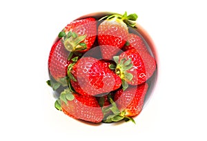 Bowl full of fresh and natural red strawberries with green leaves isolated on a seamless white background