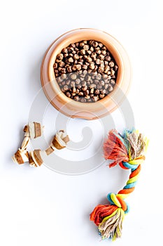 Bowl full and overflowing with dry pet - dog food bits and toys on white background top view