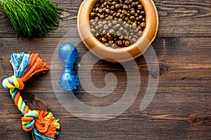 Bowl full and overflowing with dry pet - dog food bits and toys on wooden background top view mock-up