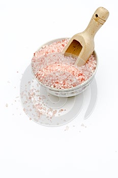 bowl full of pink bath salts, spoon, grains of salt fallen, on white background frontal view photo
