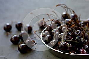 Bowl full of ripe red dark cherries on stone textured table surface as low key photo.