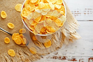 Bowl with golden flakes on a linen, on a light wooden table, next to a spoon. Rustic country style. View from above