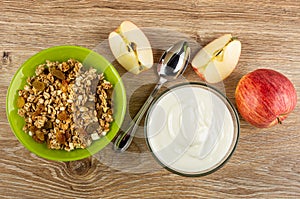 Bowl with granola, pieces of apple, spoon, bowl with yogurt on table. Top view