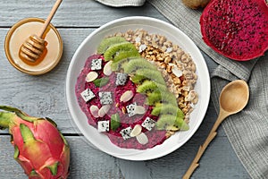 Bowl of granola with pitahaya, kiwi and almonds served on grey wooden table, flat lay