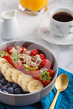 Bowl of granola with yogurt, fresh raspberries, blueberries, strawberries, banana and nuts on aqua napkin for healthy breakfast