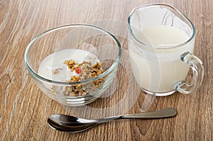 Bowl with granola and yogurt, jug of yogurt, spoon on wooden table
