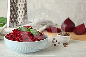 Bowl of grated boiled beets with basil and allspice on wooden table