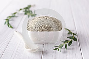 Bowl with green clay powder and fresh eucalyptus leaves on white background. Concept of face and body care.