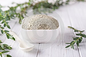 Bowl with green clay powder and fresh eucalyptus leaves on white background. Concept of face and body care.