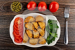 Bowl with green peas, row of  tomatoes, partitioned dish with patties, parsley, tomato, fork on table. Top view