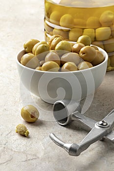Bowl with green Turkish olives close up and a olive pitter in front