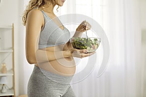 Bowl of green vegetable salad in hands of pregnant woman who monitors her diet during pregnancy.
