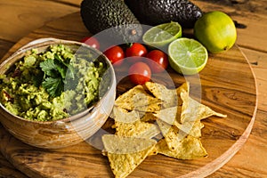 Bowl of guacamole dip with avocados tortilla chips cherry tomatoes and limes on a chopping board
