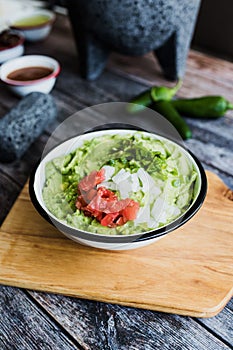 Bowl of Guacamole next to fresh ingredients on a wooden table in Mexico