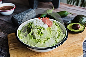 Bowl of Guacamole next to fresh ingredients on a wooden table in Mexico