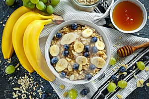 Bowl of Healthy Breakfast oatmeal with ripe blueberries, banana, honey, almonds and green grape. Top view