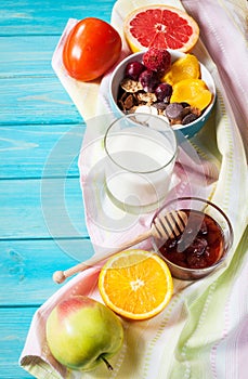 Bowl of healthy corn flakes breakfast cereal, milk and fruits on blue wood table