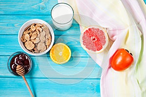 Bowl of healthy corn flakes breakfast cereal, milk and fruits on blue wood table