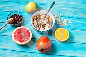 Bowl of healthy corn flakes breakfast cereal, milk and fruits on blue wood table