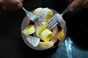 Bowl of healthy fresh fruit salad on wooden background. Man eating it with two forks.