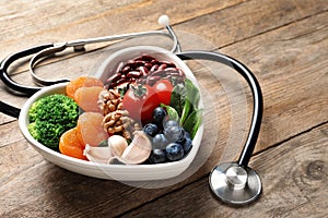 Bowl with heart-healthy diet products and stethoscope on wooden table