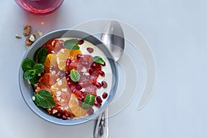 Bowl of homemade granola with yogurt, citrus and pomegranate seeds on gray wooden background. Selective focus. Healthy eating or