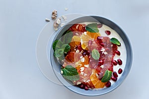 Bowl of homemade granola with yogurt, citrus and pomegranate seeds on gray wooden background. Selective focus. Healthy eating or