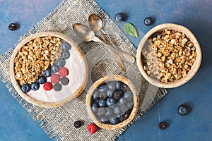 Bowl of homemade granola with yogurt and fresh berries blueberries and raspberries on blue rustic background. Healthy diet