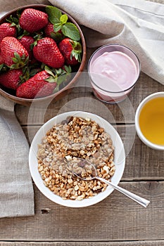 A bowl of homemade granola with yogurt and fresh strawberries on a wooden background. Healthy breakfast with green tea