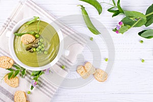 Bowl of homemade green spring pea soup topped with pumpkin seeds, croutons. On white background. flat lay.