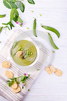 Bowl of homemade green spring pea soup topped with pumpkin seeds, croutons. On white background.