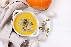 Bowl of Homemade Pumpkin and Mushrooms Soup with Cream and Pumpkin Seeds on Linen Napkin White Wooden Background Top View Copy