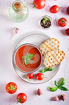 Bowl with homemade tomato soup with basil and fresh vegetables on the table. Top and vertical view