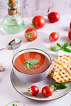 Bowl with homemade tomato soup with basil and fresh vegetables on the table. Vertical view