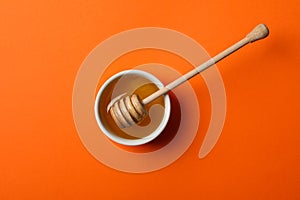 Bowl honey and dipper on orange background, top view