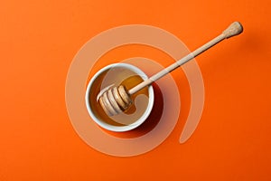 Bowl with honey and dipper on orange background, top view