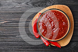 Bowl of hot chili sauce with red peppers on dark wooden background. Space for text