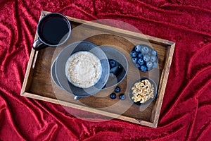 Bowl of hot oatmeal, black bowl and plate, black spoon, small bowls of blueberries and walnuts, cup of tea, red tablecloth