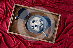Bowl of hot oatmeal with blueberries and walnuts, black bowl and plate, black spoon, cup of tea,