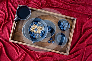 Bowl of hot oatmeal with blueberries and walnuts, black bowl and plate, black spoon, small topping bowls, cup of tea