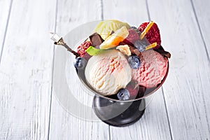 Bowl with ice cream with three different scoops of white, yellow, red colors and waffle cone, chocolate, tangerines and